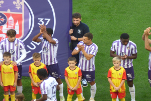 Eine Gruppe junger Jungs auf einem Fussballfeld, die klatschen, mit einem Banner und Logos im Hintergrund.