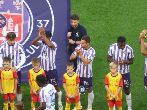 Eine Gruppe junger Jungs auf einem Fussballfeld, die klatschen, mit einem Banner und Logos im Hintergrund.