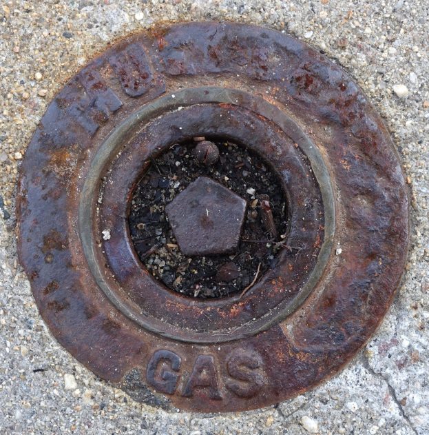 Ein verrosteter Metall-Schachtobel auf dem Boden mit dem Wort 'Gas' darauf.