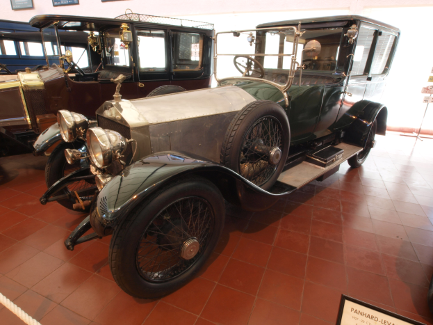 Ein klassisches Auto mit einem eleganten Design und einem glänzenden Finish, das in einem Museum ausgestellt ist, abgesperrt mit einem Seil und umgeben von Informationsschildern und gerahmten Ausstellungen.