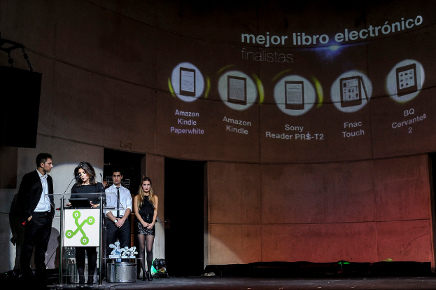 Vier Personen auf der linken Seite, wobei eine Frau einen Vortrag hält und im Hintergrund Bilder von Geräten mit ihren Namen darunter zu sehen sind.