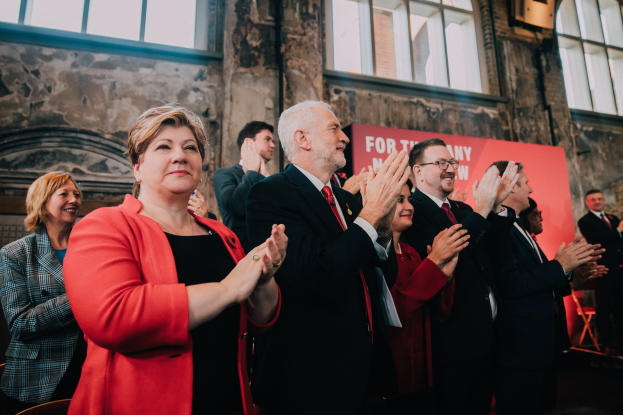 Eine Gruppe von Menschen, die vor einer Menge jubeln und eine Wahlsieg-Banner im Hintergrund haben.