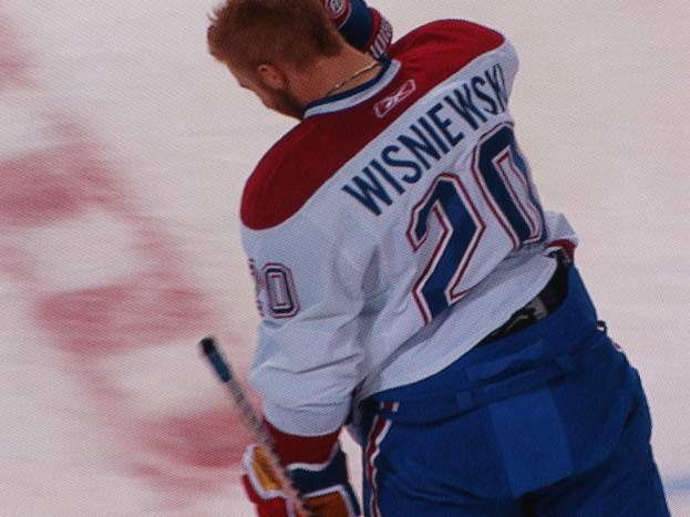 Professioneller Eishockeyspieler in einem "Wisniewski"-Trikot auf dem Eis stehend, einen Eishockeyschläger haltend mit konzentrierter Miene.