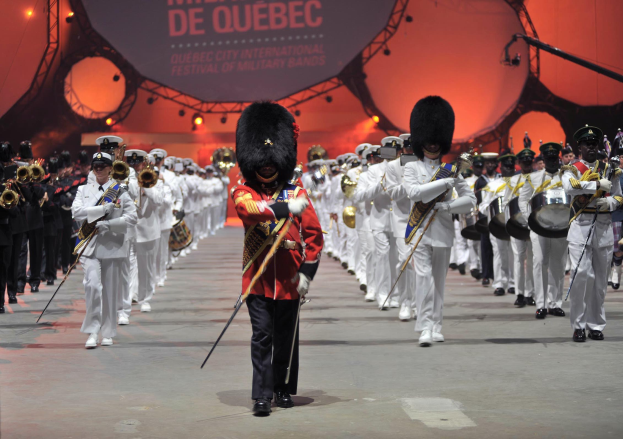 Eine Gruppe uniformierter Musiker marschiert im Gleichschritt, einige spielen Instrumente, während die Eröffnungszeremonie des Montreal International Festival of Military Bands stattfindet.