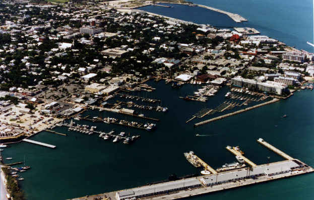 Ein Überblick über eine Stadt mit zahlreichen Gebäuden und Meerwasser, der einen Hafen mit Schiffen an der vorderen Unterseite zeigt.