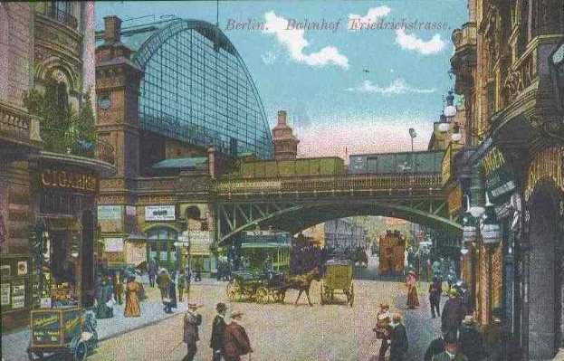 Alte Postkarte zeigt eine belebte Berliner Straße mit Führer, Kutschen, Gebäuden, Laternen, einer Brücke und einem bewölktem Himmel mit Text oben.
