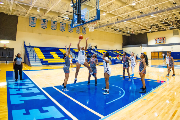 Eine Gruppe von Frauen, die Basketball in einer Turnhalle mit einem Scoreboard spielt, das ihren NCAA-Turniersieg anzeigt.