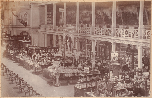 Ein altes Schwarz-Weiß-Foto eines Ladens, der mit verschiedenen Möbelstücken gefüllt ist, darunter Tische, Stühle, Säulen, Geländer, Statuen und Fotorahmen an den Wänden.