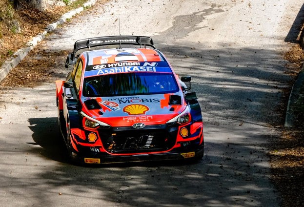 Ein rotes und weißes Rallyeauto mit Textmarkierungen fährt auf einer bewaldeten, kurvenreichen Straße während der 2018 FIA World Rally Championship.