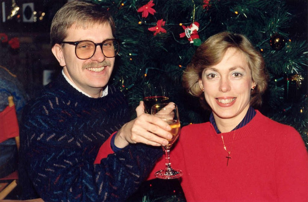 Ein Paar lächelt beim Weintrinken mit einem Weihnachtsbaum im Hintergrund.