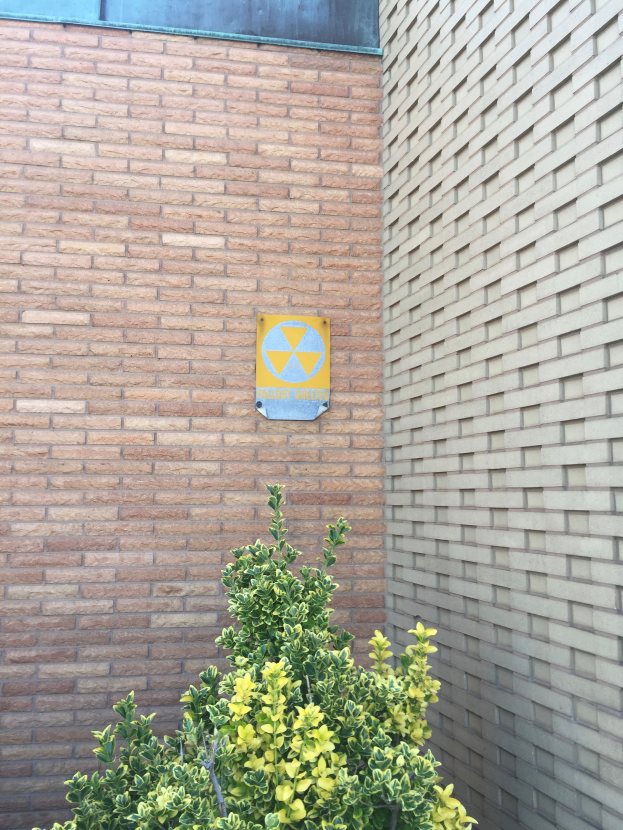 Ein Ziegelgebäude mit einem Strahlensymbol-Schild, einer Pflanze am Boden und einer Tafel an der Wand, die darauf hinweist, dass es sich um ein Kernkraftwerk handelt.