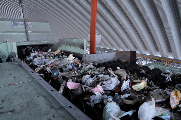 Pinkes Gebäude mit einem zentralen Uhrenturm, umgeben von Fenstern, Schirmen, einem Schild, einer Straßenlaterne, Topfpflanzen und einem bewölkten Himmel, das Attraktionen in München, Deutschland, darstellt.