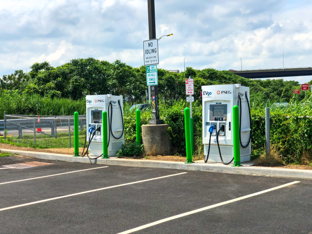Elektrische Fahrzeug-Ladestation auf einem Parkplatz mit umgebenen Infrastruktur und einer Brücke im Hintergrund.