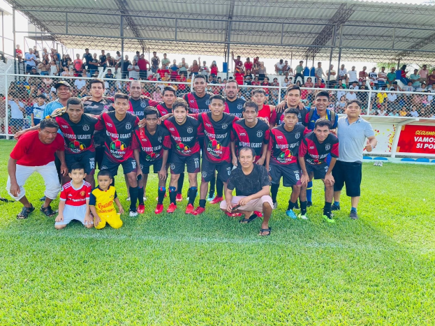 Gruppe von Männern feiert auf einem Fußballfeld mit einem Siegesschild, auf dem "Fotos Ugarte U-17 vs U-18" steht, unter einem bewölkten Himmel.