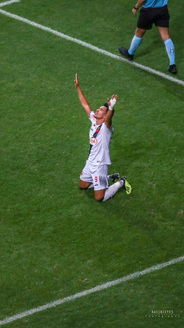 Ein Fussballspieler kniet auf dem Boden und feiert mit ausgestreckten Armen, trägt eine Sportuniform und Stiefel.