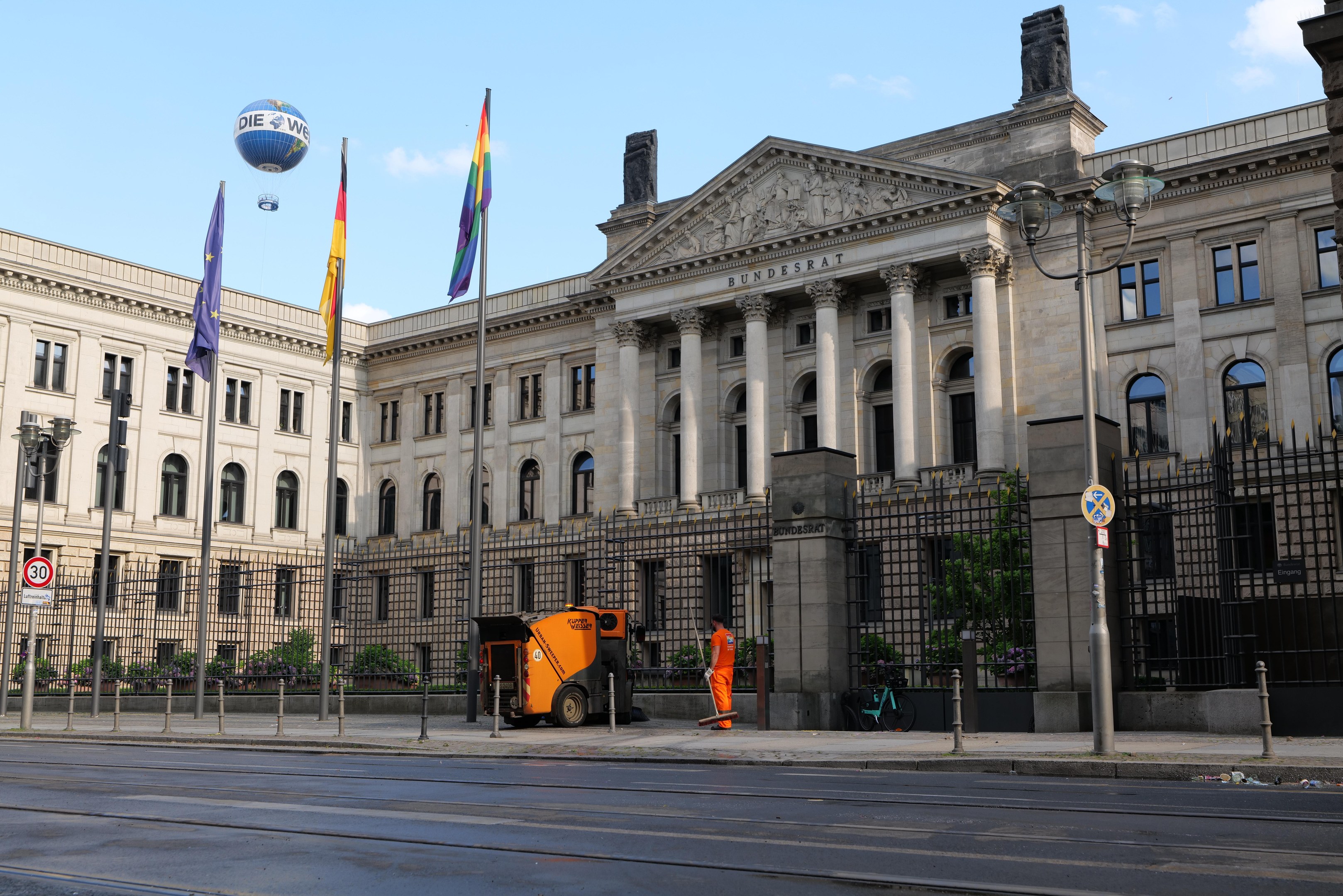 Großes modernes Gebäude mit vielen Fenstern, als der Bundestag in Berlin identifiziert, umgeben von Straßeninfrastruktur, Fußgängern und Bäumen unter einem bewölkten Himmel.