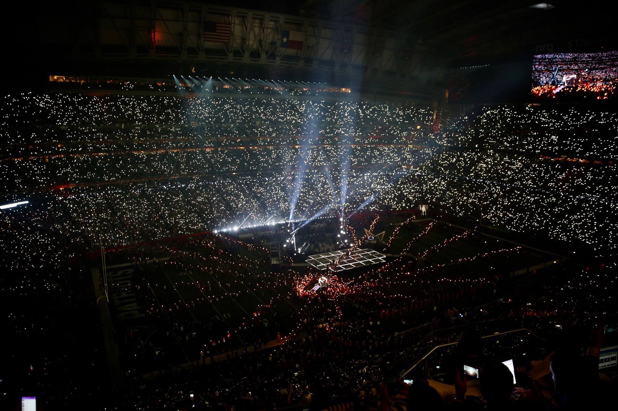 Große Menschenmenge in einem hell erleuchteten Stadion bei Nacht mit einem Bildschirm, der links die Ergebnisse des Super Bowl XLVII-Halbtzeitshows anzeigt.
