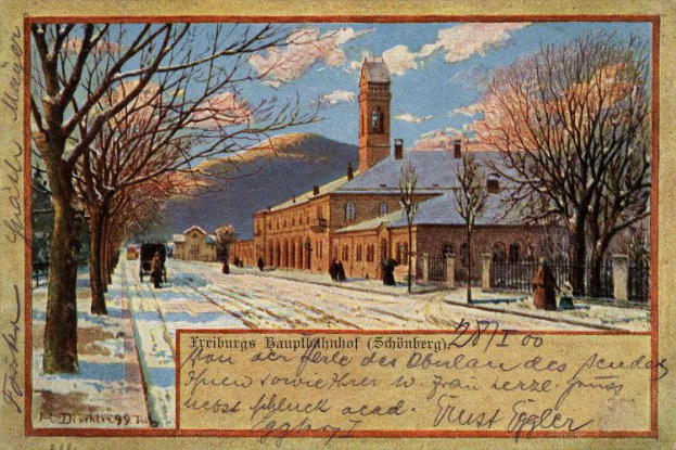 Eine alte Postkarte, die ein schneebedecktes Gebäude zeigt, das von Bäumen, Menschen und einem Zaun umgeben ist, mit der Aufschrift "Freiburg Hauptbahnhof" unten.