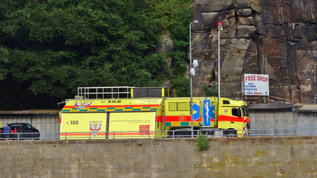 Ambulanz neben einer Straße an einem Felsen geparkt, mit verschiedenen Straßenobjekten und Bäumen im Hintergrund.