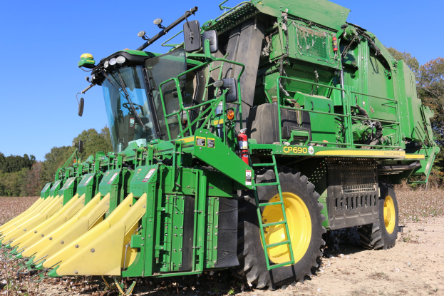 Ein großer grüner und gelber Mähdrescher auf einem Feld umgeben von Bäumen unter einem klaren blauen Himmel.