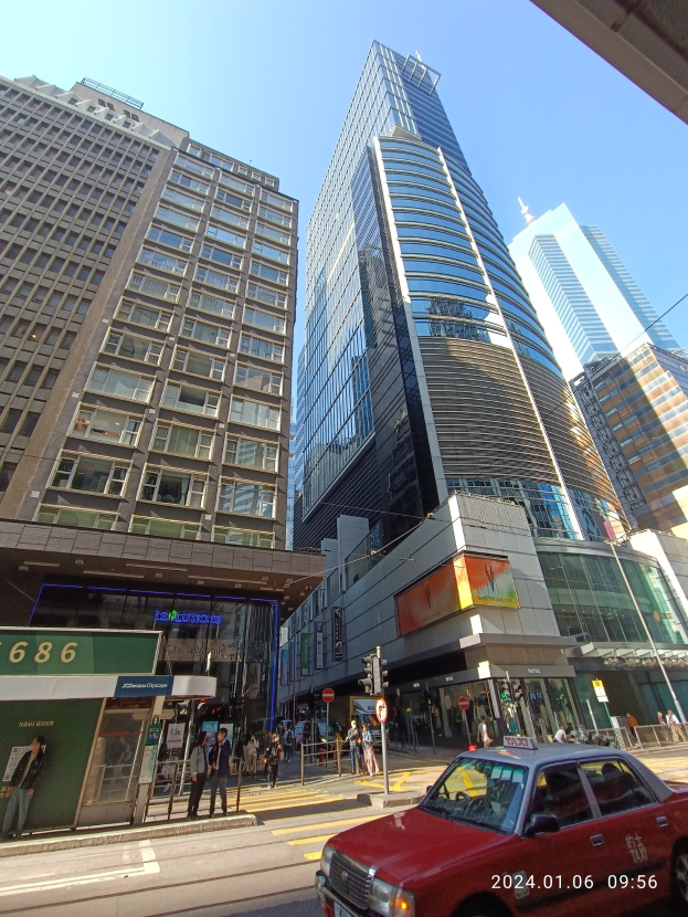 Ein rotes Auto fährt eine Stadtstraße entlang, die von hohen Wolkenkratzern gesäumt ist, mit Fußgängern, Verkehrsampeln und Schildern.