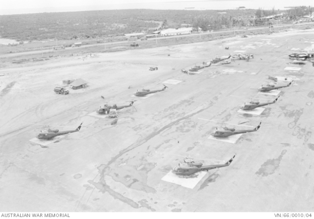 Mehrere Militärhubschrauber auf dem Boden umgeben von Fahrzeugen, Schuppen, Polen, Bäumen und Wasser, mit Text am unteren Bildrand.