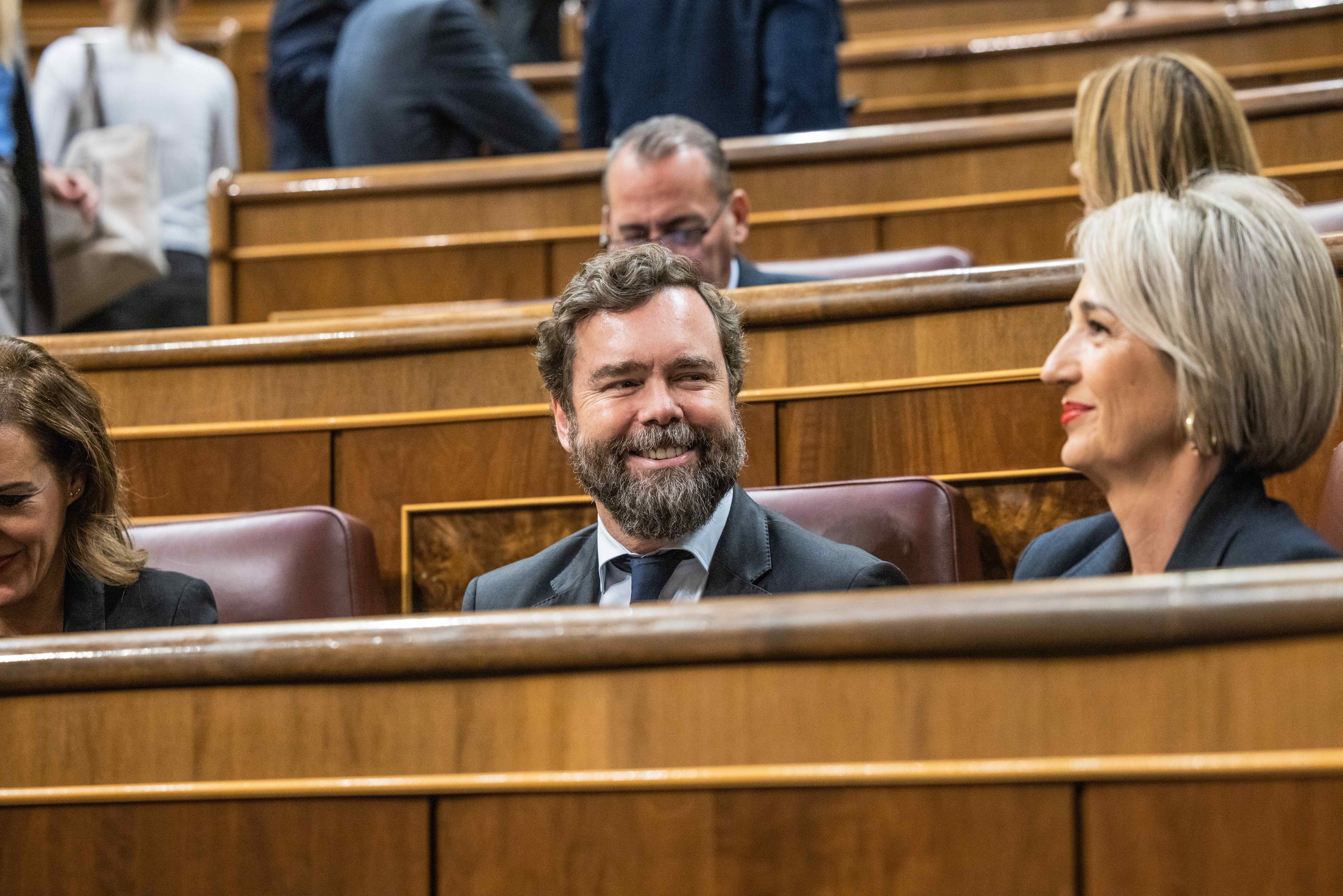 Ein Mann im Anzug und zwei leger gekleidete Frauen sitzen zusammen in einem Gerichtssaal mit Bänken im Hintergrund.