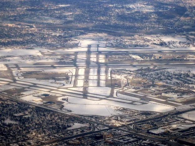 Luftaufnahme eines Flughafens in einer verschneiten Stadt mit Straßen, Gebäuden und Bäumen.