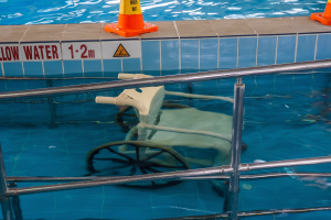 Ein Schwimmbad mit einem Stuhl in der Mitte, umgeben von Sicherheitskegeln und einem Geländer, und ein Schild an der Wand, das auf die Anwesenheit von Schwimmausrüstung hinweist.