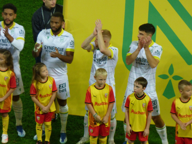 Eine Gruppe von Fuballspielern in Uniformen, die auf einem Feld klatschen, mit einem "Ligue 1"-Schild im Hintergrund, feiern einen Sieg.