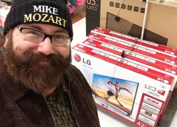 Eine Person, die vor Fernsehgeräten lächelt, die in Kartons verpackt sind und andere Gegenstände.