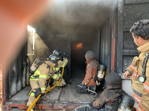Eine Gruppe von Feuerwehrleuten auf der Ladefläche eines Trucks, mit Helmen und Zylindern bekleidet, wobei einer eine Rohrleitung hält.