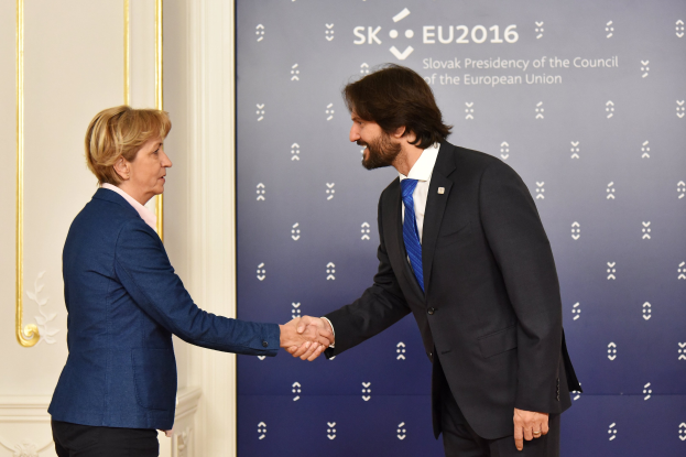Bundeskanzlerin Angela Merkel und Bundeskanzler Joachim Gauck schütteln sich lachend vor einem "EU-Gipfel"-Plakat mit einer Tür im Hintergrund die Hände.