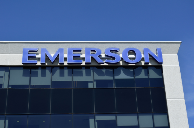 Das Emerson-Logo ist auf der Seite eines Gebäudes mit dem Text "Emerson investiert 1,5 Milliarden US-Dollar in den USA" darunter zu sehen, vor einem klaren blauen Himmel.