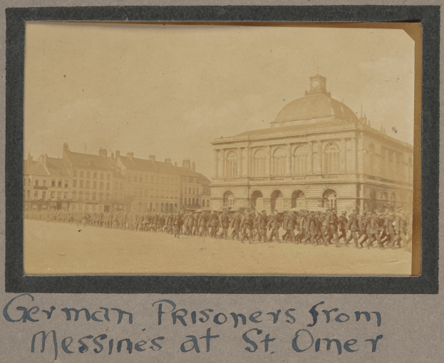 Eine Gruppe deutscher Gefangener aus Messines steht vor einem Gebäude an einem klaren blauen Himmel, mit Text am unteren Bildrand.