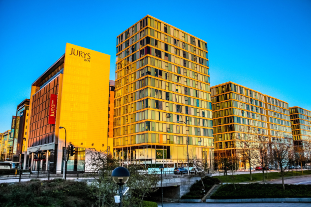Lebendige Stadtkulisse des Jurys Inn Birmingham City Centre mit hohen Gebäuden, Fahrzeugen, Grünflächen und wolkenlosem Himmel.