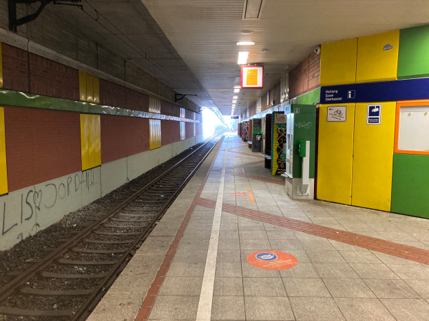 Ein Bahnhof in Berlin, Deutschland, mit einem Zug auf den Schienen, beleuchteter Deckenlampen, Graffiti an der linken Wand und einigen Gegenständen auf der rechten Seite.