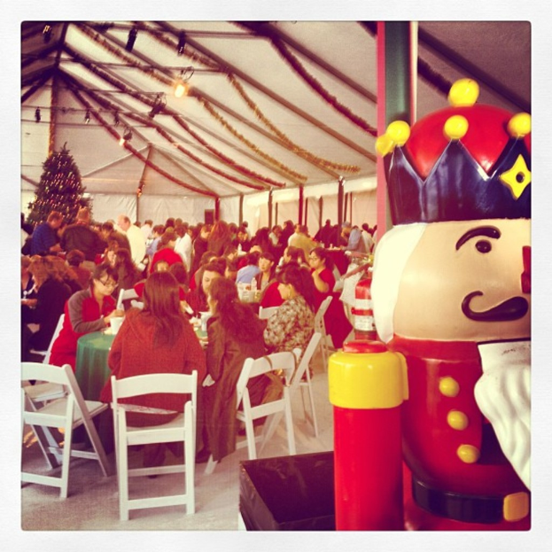 Eine Gruppe von Menschen feiert Weihnachten in einer Hütte, mit einem geschmückten Baum und weißen Stühlen, ein roter Spielzeug-Sicherheitsmann mit einer schwarzen Krone.