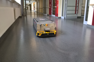 Ein Roboter, der zum Bodenreinigen entworfen wurde, steht auf dem Boden eines Gebäudes und ist von Wänden, Türen, Lampen und anderen Gegenständen umgeben.