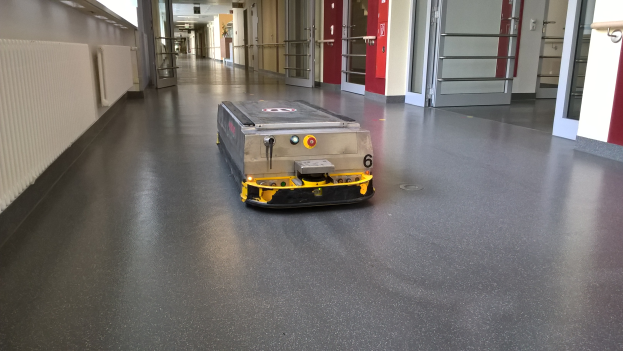 Ein Roboter, der zum Bodenreinigen entworfen wurde, steht auf dem Boden eines Gebäudes und ist von Wänden, Türen, Lampen und anderen Gegenständen umgeben.