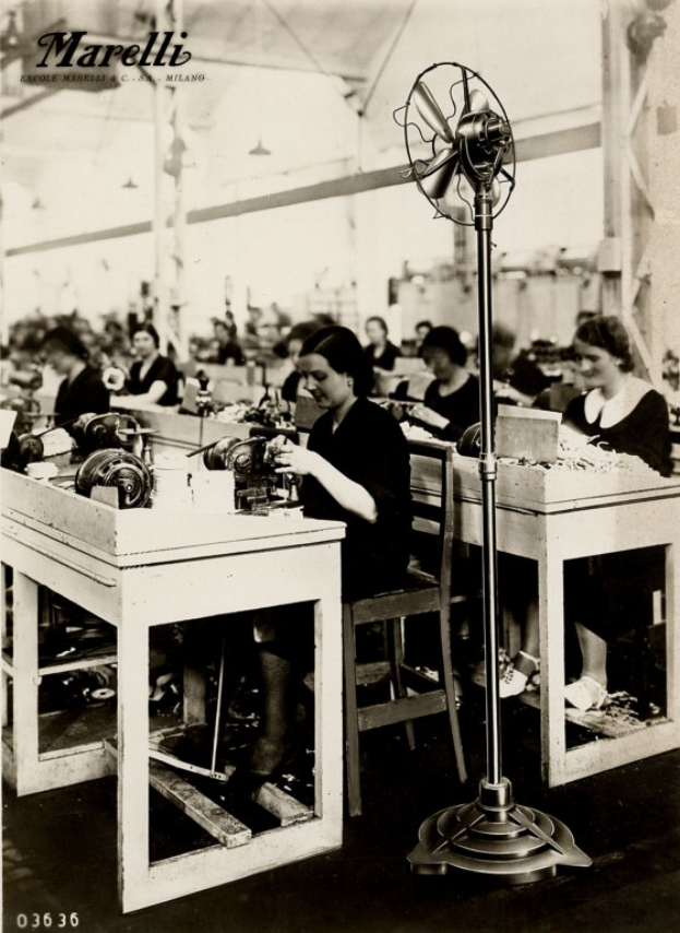 Ein Schwarz-Weiß-Foto von Frauen, die an Nähmaschinen in einer Fabrik arbeiten, mit einem Tischventilator im Vordergrund und Text oben.