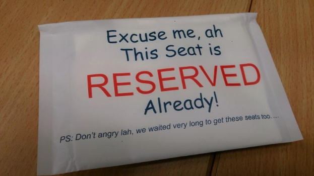 Ein hölzerner Tisch mit einem Papierzettel, auf dem steht: "Entschuldigung, dieser Sitz ist bereits reserviert."