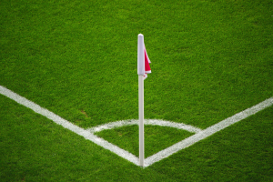Ein Fuballfeld mit grünem Gras, weißen Begrenzungslinien und einem weißen Pfahl mit einer rot-weißen Flagge auf dem zentralen Strafpunkt.