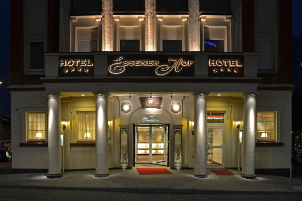 Das Essenerhof Hotel in Berlin, Deutschland, ein mehrstöckiges Gebäude mit Fenstern, Türen, Säulen und einem Namensschild, das sich auf einer Straße mit Fahrzeugen auf der rechten Seite und einem klaren Himmel im Hintergrund befindet.