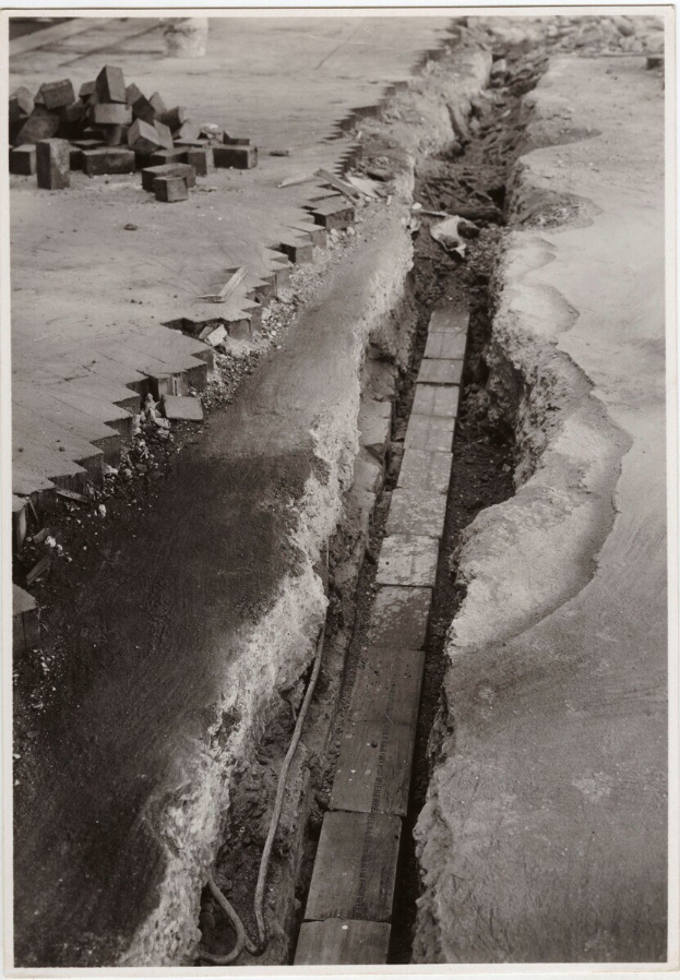 Ein Schwarz-Weiß-Foto einer gebrochenen Straße mit zerstreuten Ziegeln auf der linken Seite.