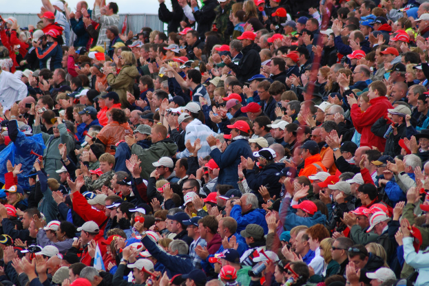 Eine große Menschenmenge, viele mit roten Mützen, versammelte sich vor einem eingezäunten Bereich.