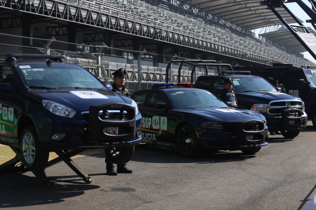Polizeiautos vor einer Rennstrecke geparkt mit uniformierten Personen, Stadion mit Geländern und Maschendrahtzaun im Hintergrund.