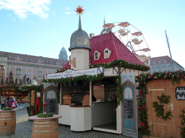 Kleines rotes Gebäude mit einem Riesenrad davor, umgeben von Festdekorationen und Menschen bei einer Oktoberfest-Feier in München, Deutschland.