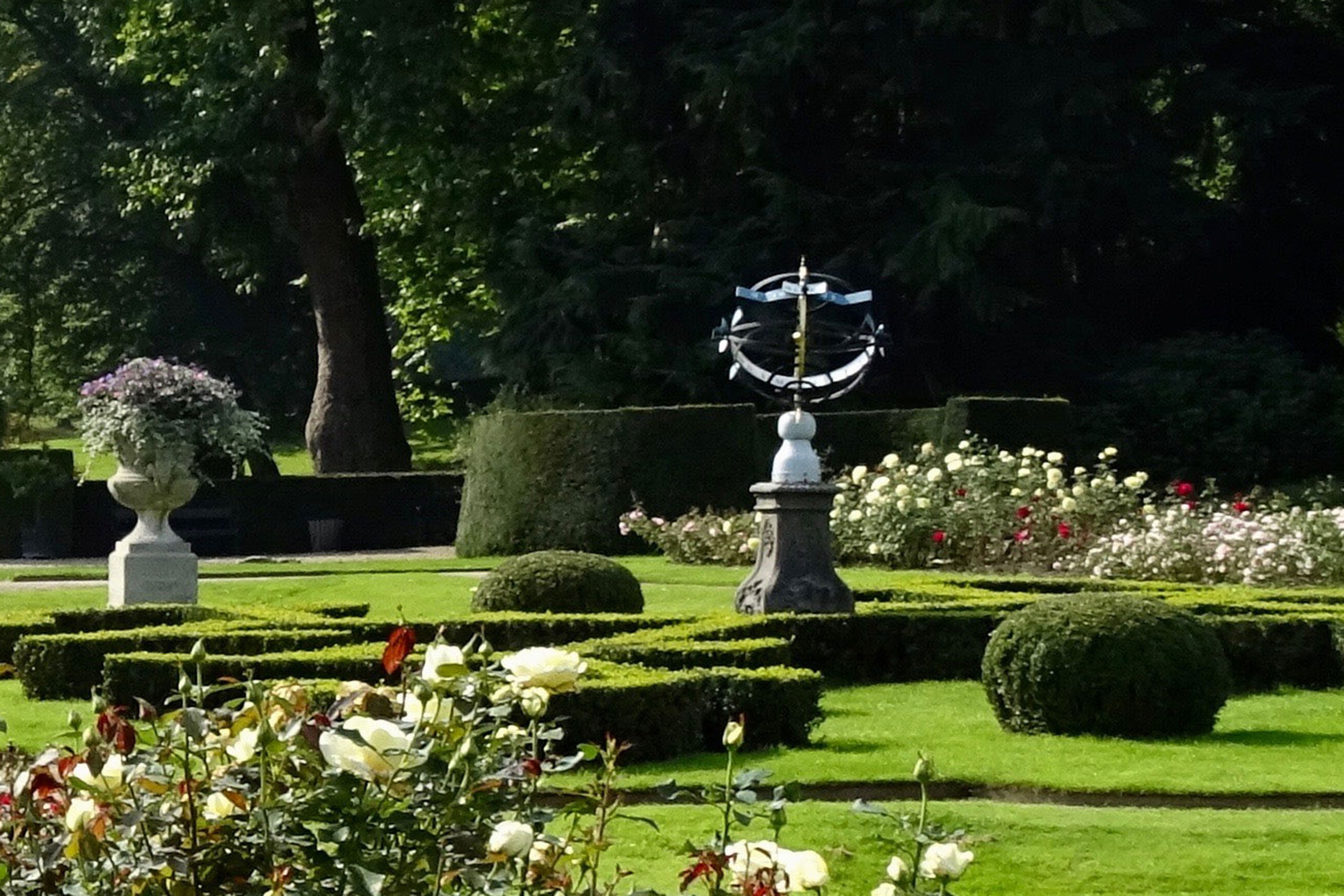 Ein üppiger Garten mit verschiedenen Pflanzen, Blumen, Gras und Bäumen, mit einer zentralen Statue, gelegen in den Royal Botanic Gardens in Edinburgh, Schottland.