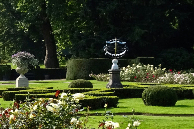 Ein üppiger Garten mit verschiedenen Pflanzen, Blumen, Gras und Bäumen, mit einer zentralen Statue, gelegen in den Royal Botanic Gardens in Edinburgh, Schottland.
